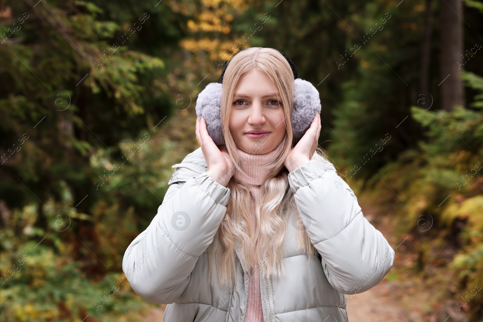 Photo of Young beautiful woman wearing warm earmuffs in forest