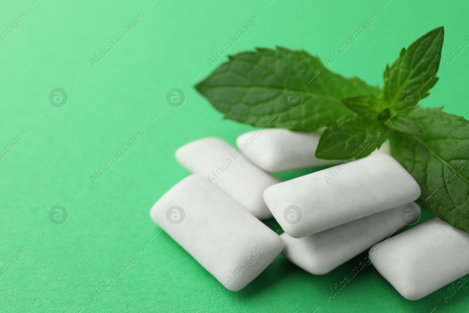 Photo of Tasty white chewing gums and mint leaves on green background, closeup. Space for text
