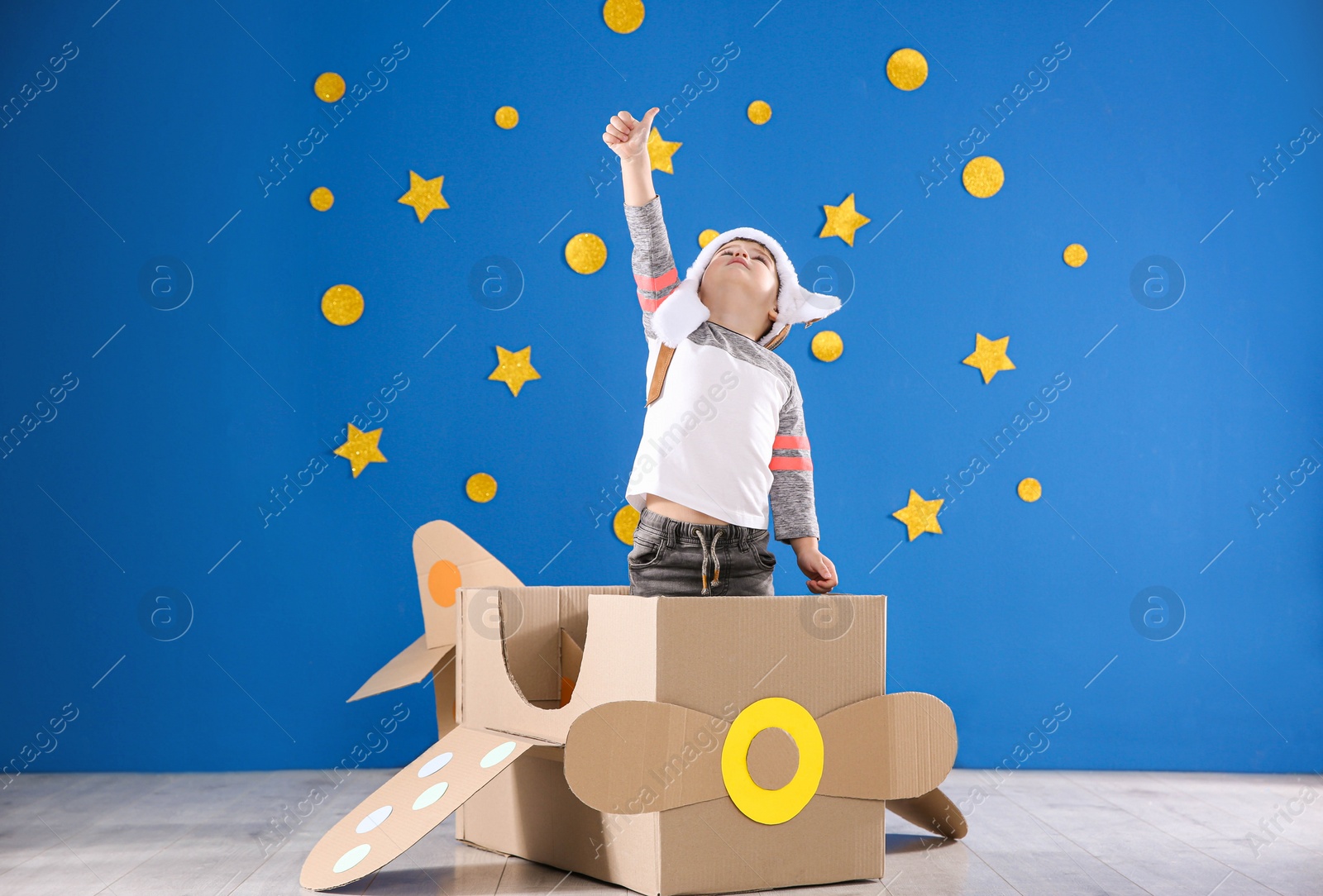 Photo of Cute little child playing with cardboard airplane near blue wall