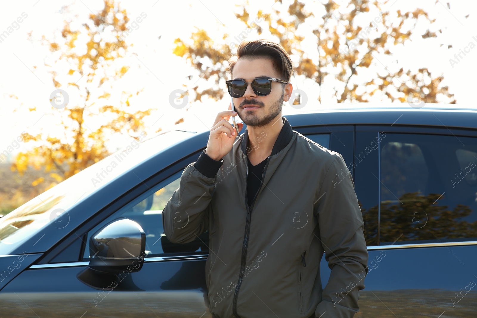 Photo of Young man talking on phone near modern car, outdoors