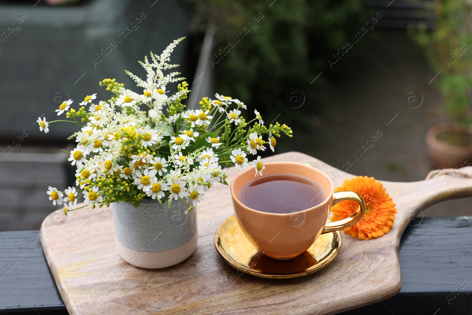 Photo of Cup of delicious chamomile tea and fresh flowers outdoors