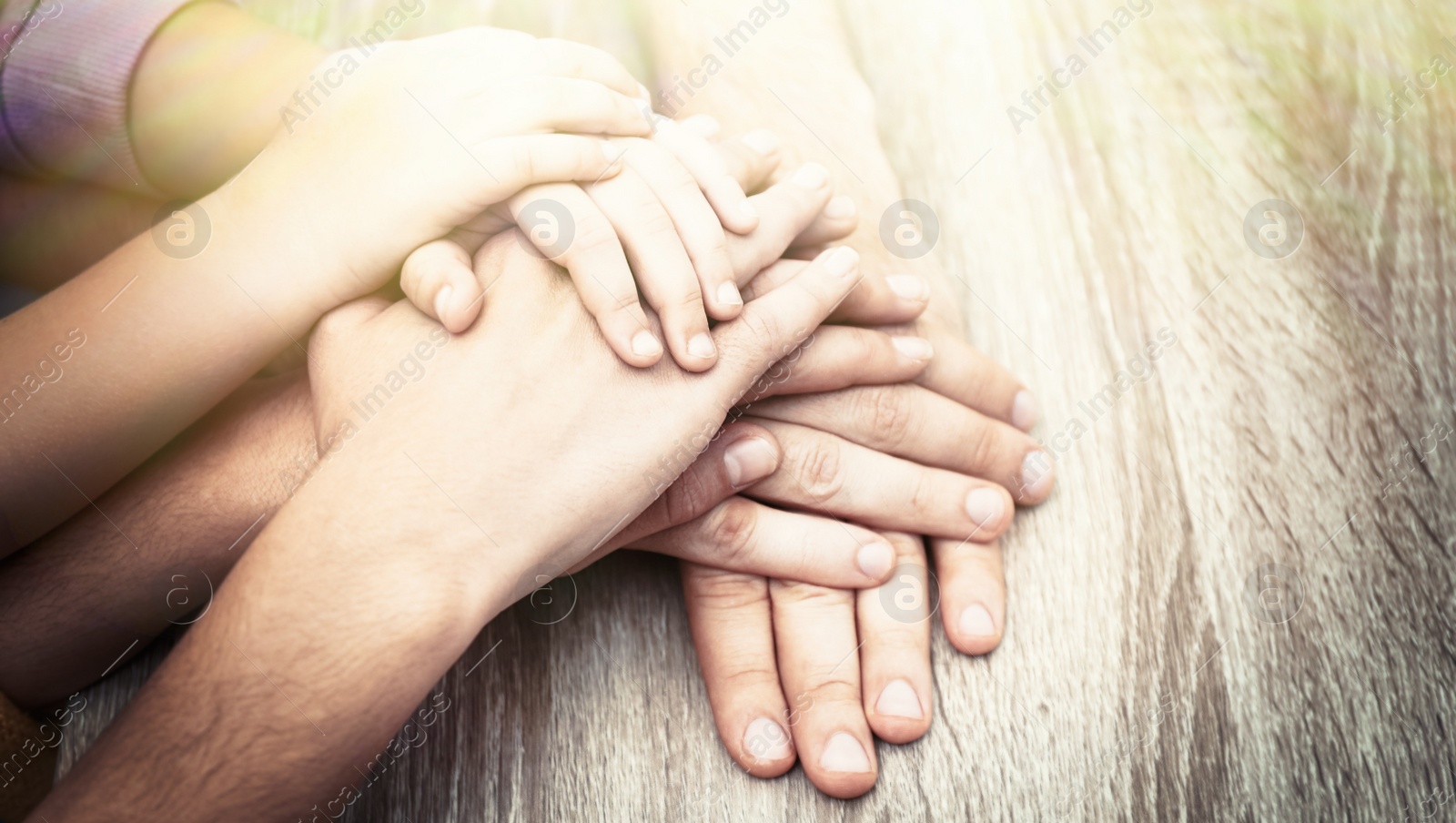Image of Happy family holding hands at wooden table indoors, closeup. Banner design 