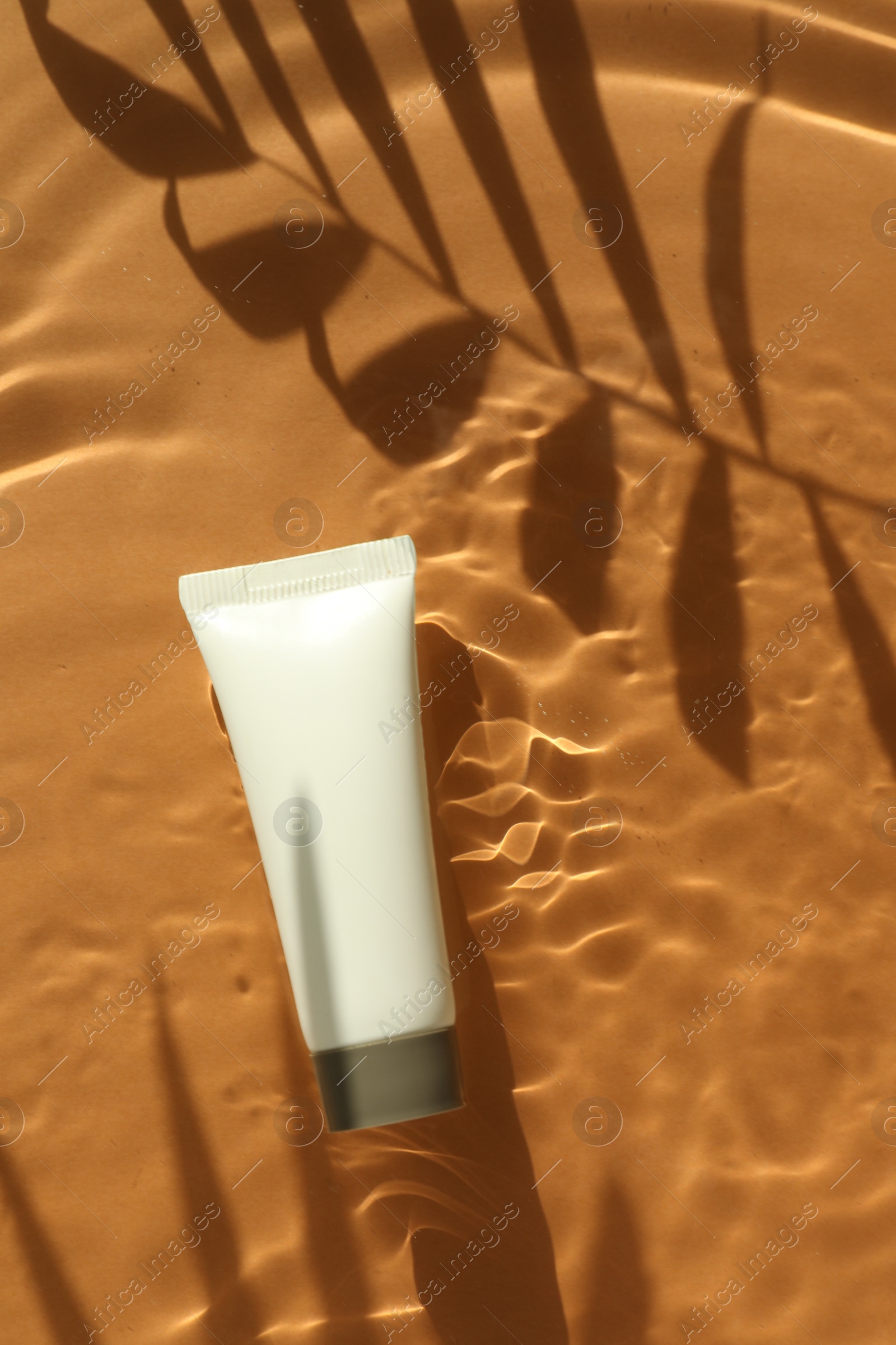 Photo of Tube with moisturizing cream in water and shadows from palm leaves on orange background, top view