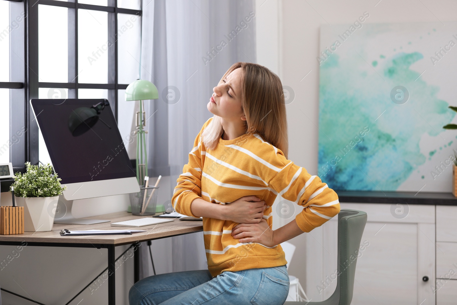 Photo of Young woman suffering from back pain in office