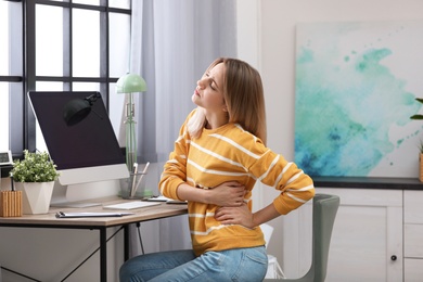 Photo of Young woman suffering from back pain in office