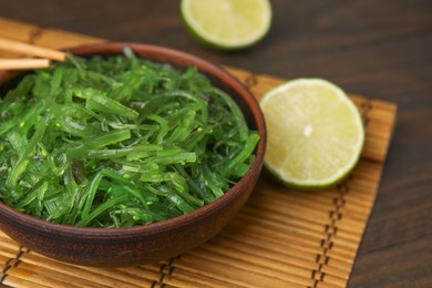 Photo of Tasty seaweed salad in bowl served on wooden table, closeup