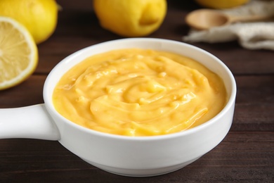 Photo of Delicious lemon curd in saucepan on dark wooden table, closeup
