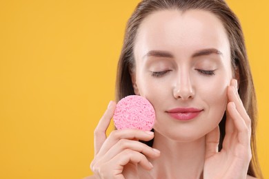 Photo of Happy young woman washing her face with sponge on orange background. Space for text