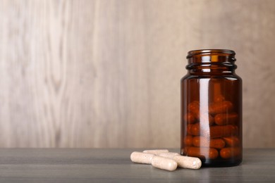 Photo of Gelatin capsules and bottle on wooden table, space for text