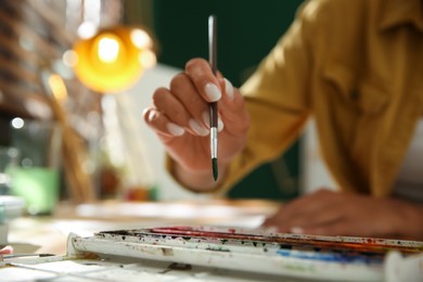 Photo of Young woman drawing with watercolors at table, closeup