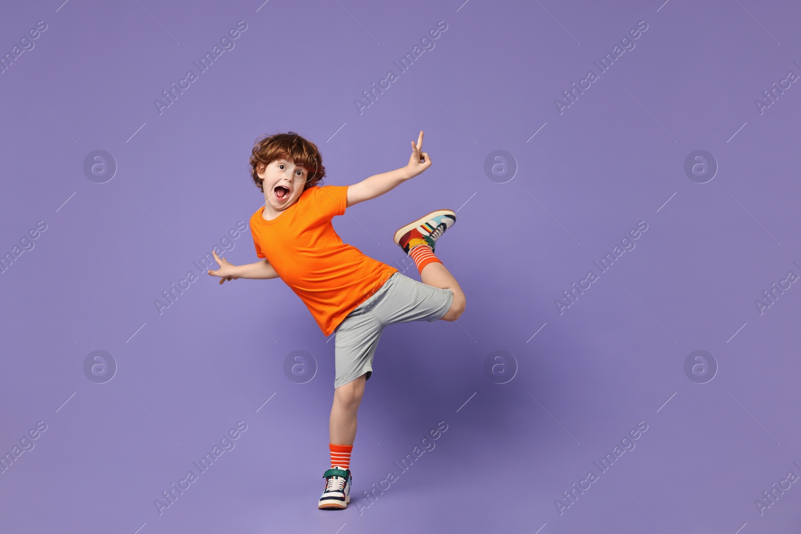 Photo of Happy little boy dancing on violet background