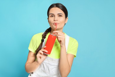 Photo of Beautiful happy woman drinking from red beverage can on light blue background