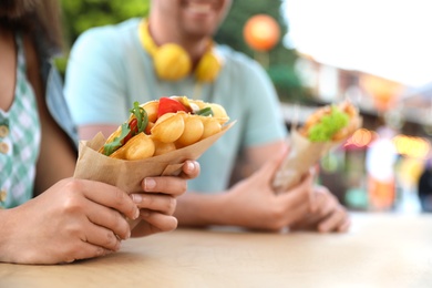 Photo of Young couple holding delicious bubble waffles with tomato and arugula at table outdoors, closeup