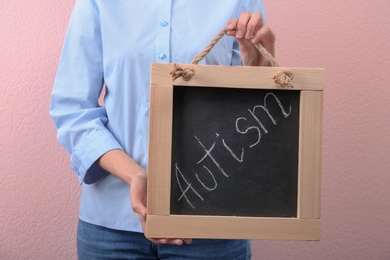 Photo of Woman holding blackboard with word "Autism" on color background