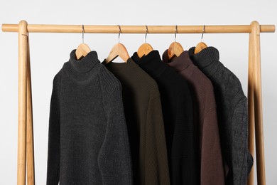 Photo of Rack with different casual sweaters on light background