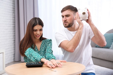 Unhappy young couple with piggy bank and money at home. Financial problems