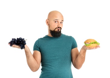 Overweight man with hamburger and grapes on white background