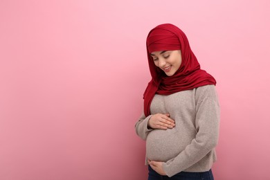 Photo of Portrait of pregnant Muslim woman in hijab on pink background, space for text