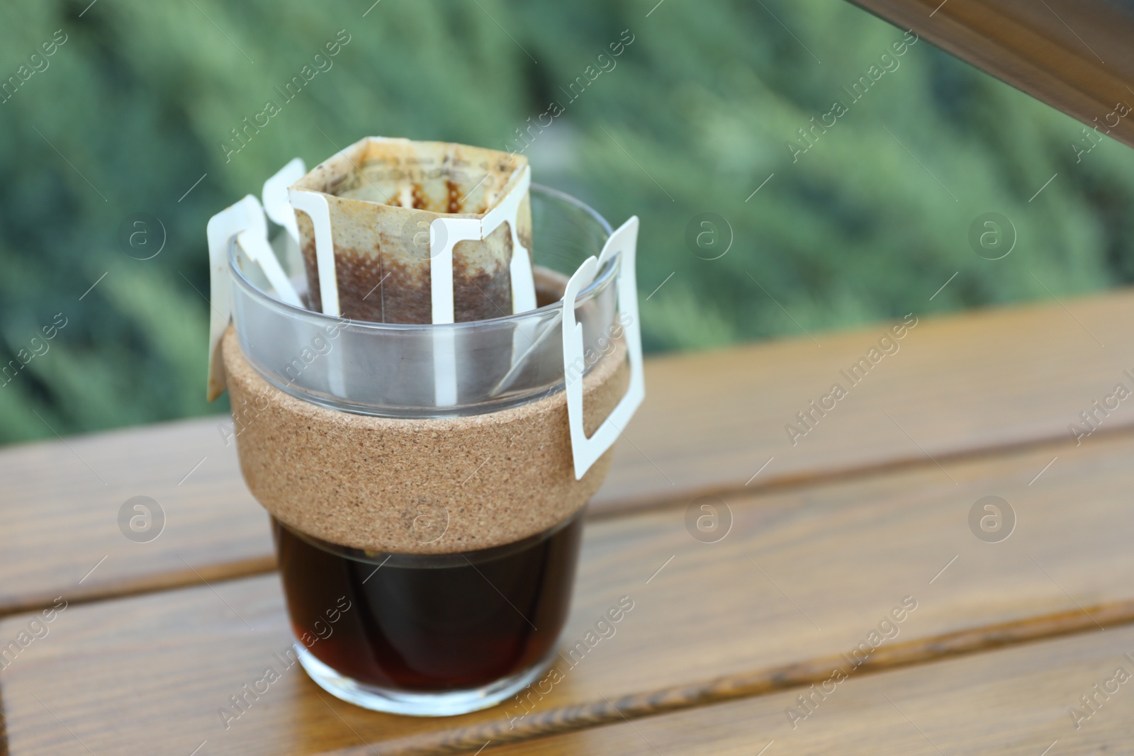 Photo of Glass cup with drip coffee bag on wooden table, closeup