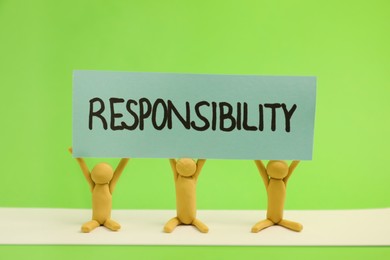 Photo of Three plasticine human figures holding card with word Responsibility on green background