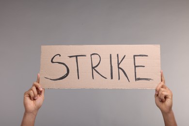 Photo of Man holding cardboard banner with word Strike on grey background, closeup