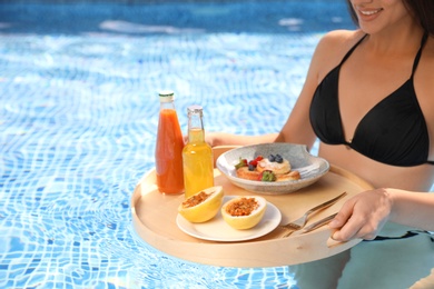 Young woman with delicious breakfast on tray in swimming pool, closeup. Space for text
