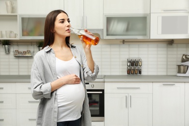 Photo of Future mother drinking alcohol in kitchen. Bad habits during pregnancy