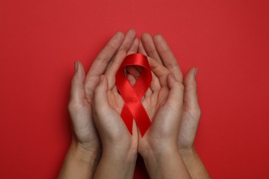 Woman and girl holding red ribbon on bright background, top view. AIDS disease awareness