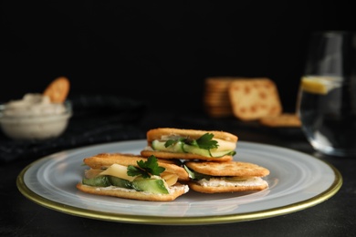 Delicious crackers with cream cheese, cucumber and parsley on black table, closeup