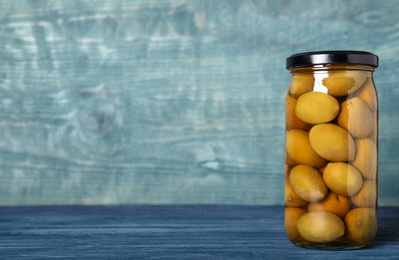 Photo of Glass jar of pickled olives on blue wooden table. Space for text