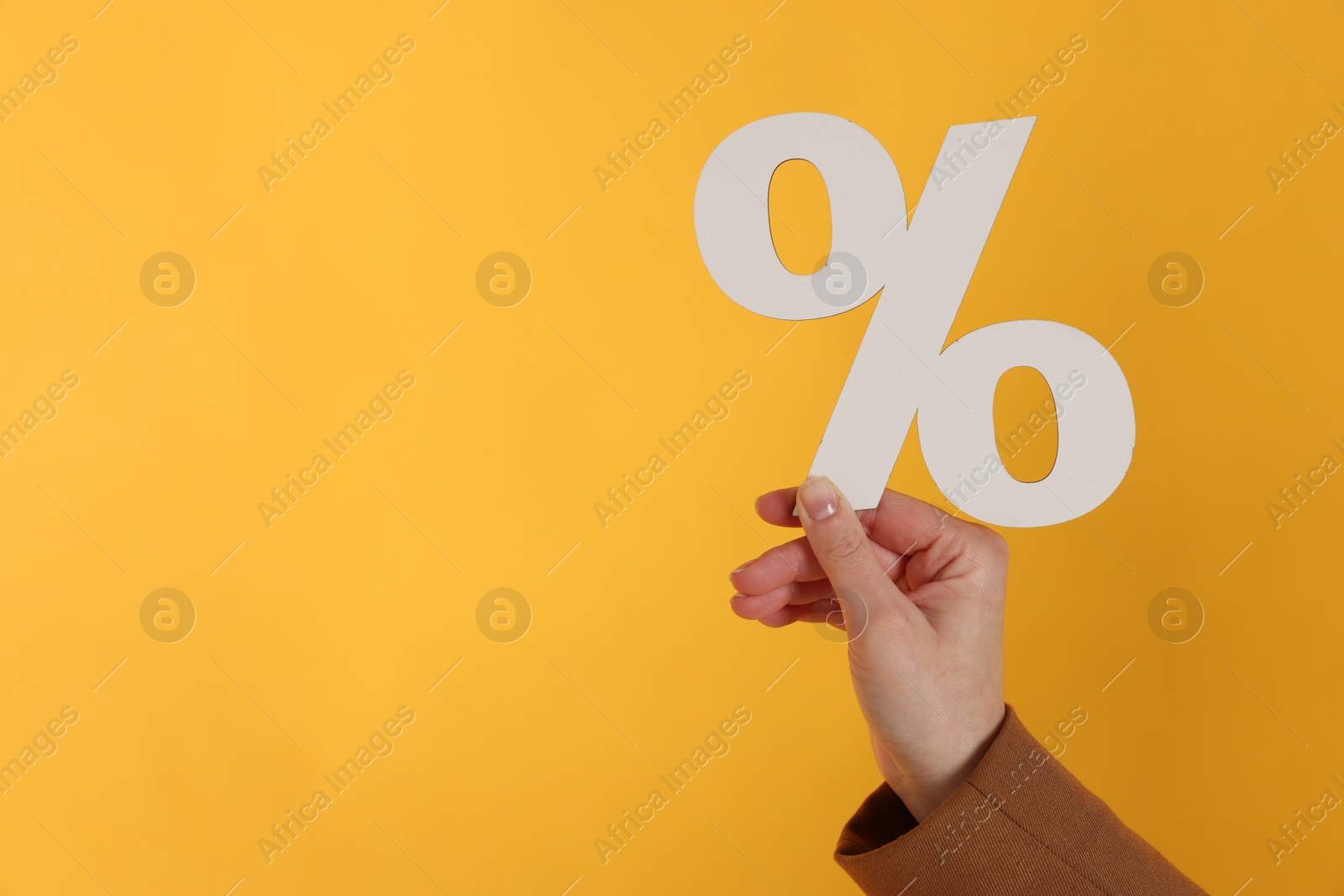 Photo of Woman holding percent sign on orange background, closeup. Space for text