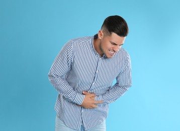 Photo of Man suffering from stomach ache on light blue background. Food poisoning