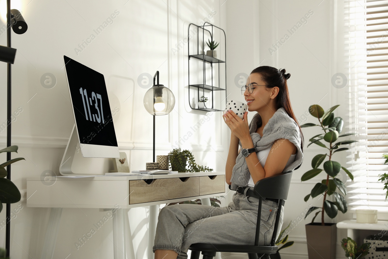 Photo of Young woman with cup of tea working at table in light room. Home office