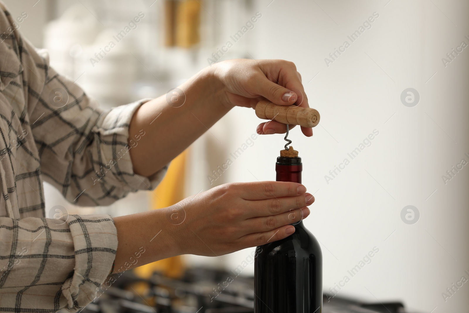 Photo of Woman opening wine bottle with corkscrew indoors, closeup