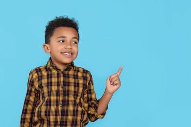 Photo of Cute African-American boy pointing on turquoise background. Space for text