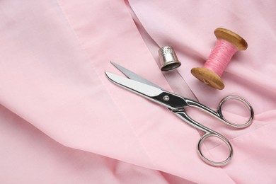 Photo of Thimble, scissors and sewing thread on pink cloth, flat lay. Space for text