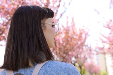 Young woman in park with beautiful blossoming sakura trees, space for text