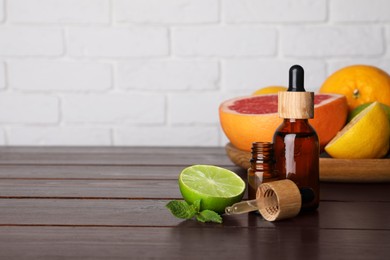 Bottles of essential oils with different citrus fruits and mint on wooden table against white brick wall. Space for text