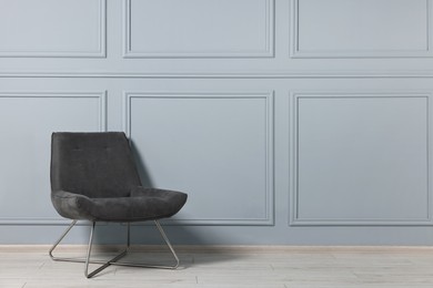 Comfortable armchair near grey wall in room, space for text