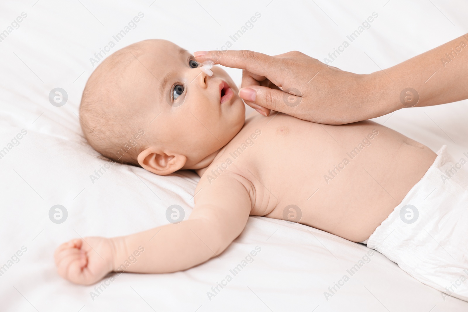 Photo of Woman applying cream onto baby`s face on bed, closeup