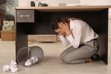 Scared young woman hiding under office desk during earthquake