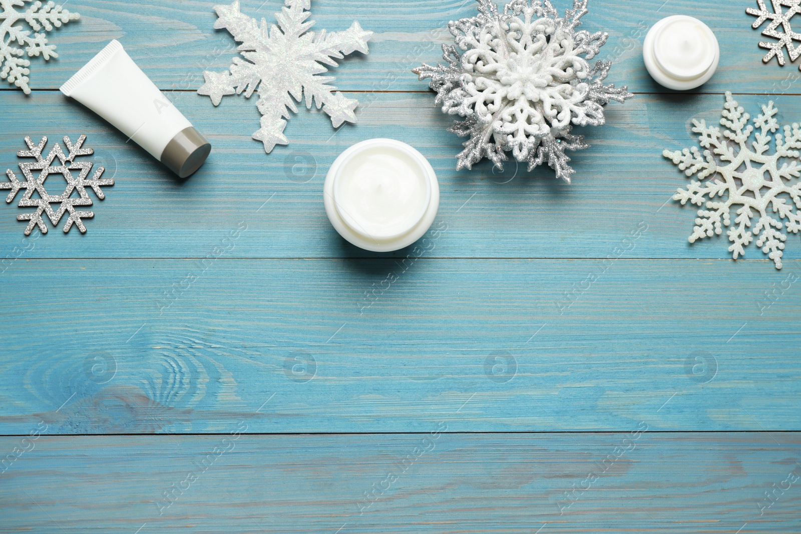 Photo of Flat lay composition with cosmetic products and snowflakes on turquoise wooden table, space for text. Winter skin care