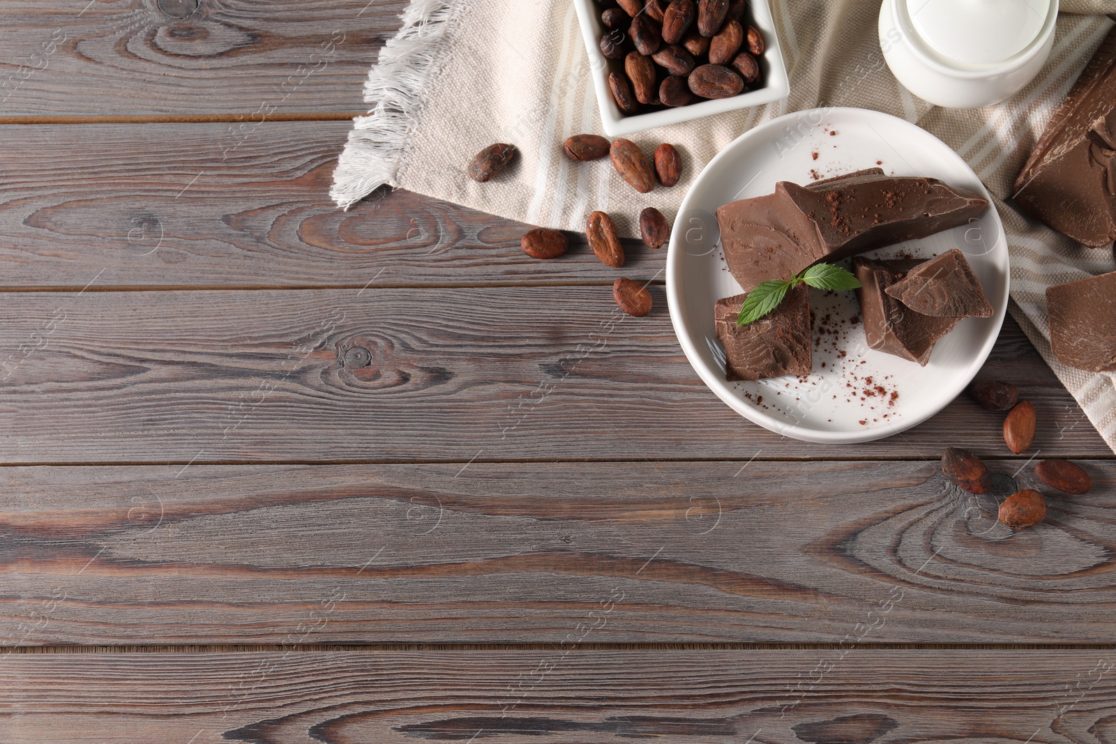Photo of Pieces of tasty milk chocolate, cocoa beans, powder and mint on wooden table, flat lay. Space for text