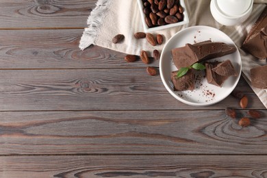 Photo of Pieces of tasty milk chocolate, cocoa beans, powder and mint on wooden table, flat lay. Space for text