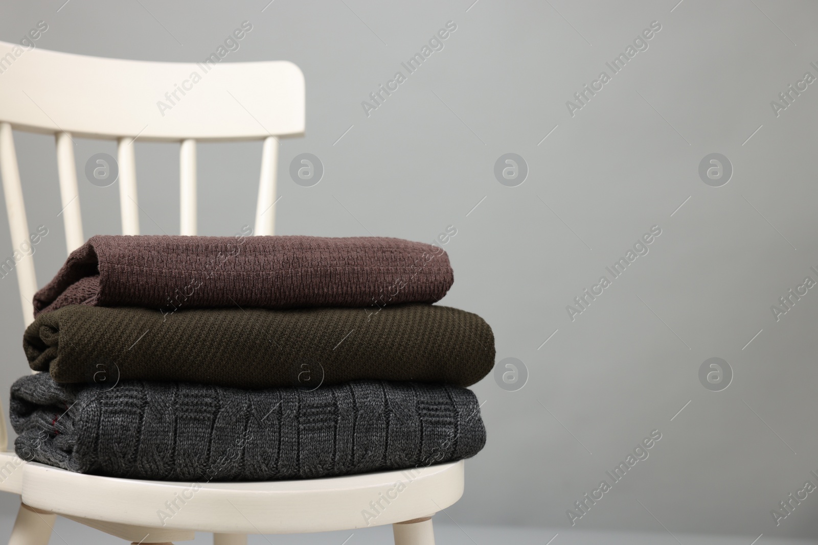 Photo of Stack of different warm sweaters on white chair against grey background. Space for text