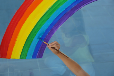 Little girl drawing rainbow on light blue background, closeup. Stay at home concept