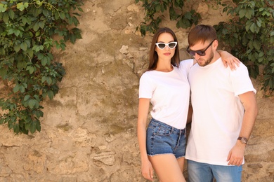 Photo of Young couple wearing white t-shirts near stone wall on street