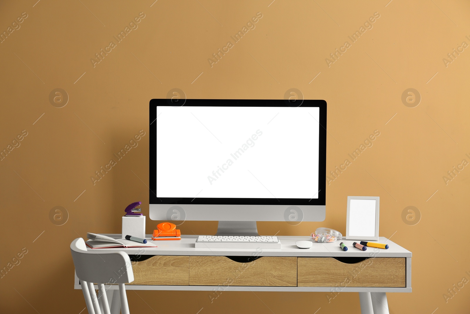 Photo of Stylish workplace with computer and stationery on wooden table near beige wall