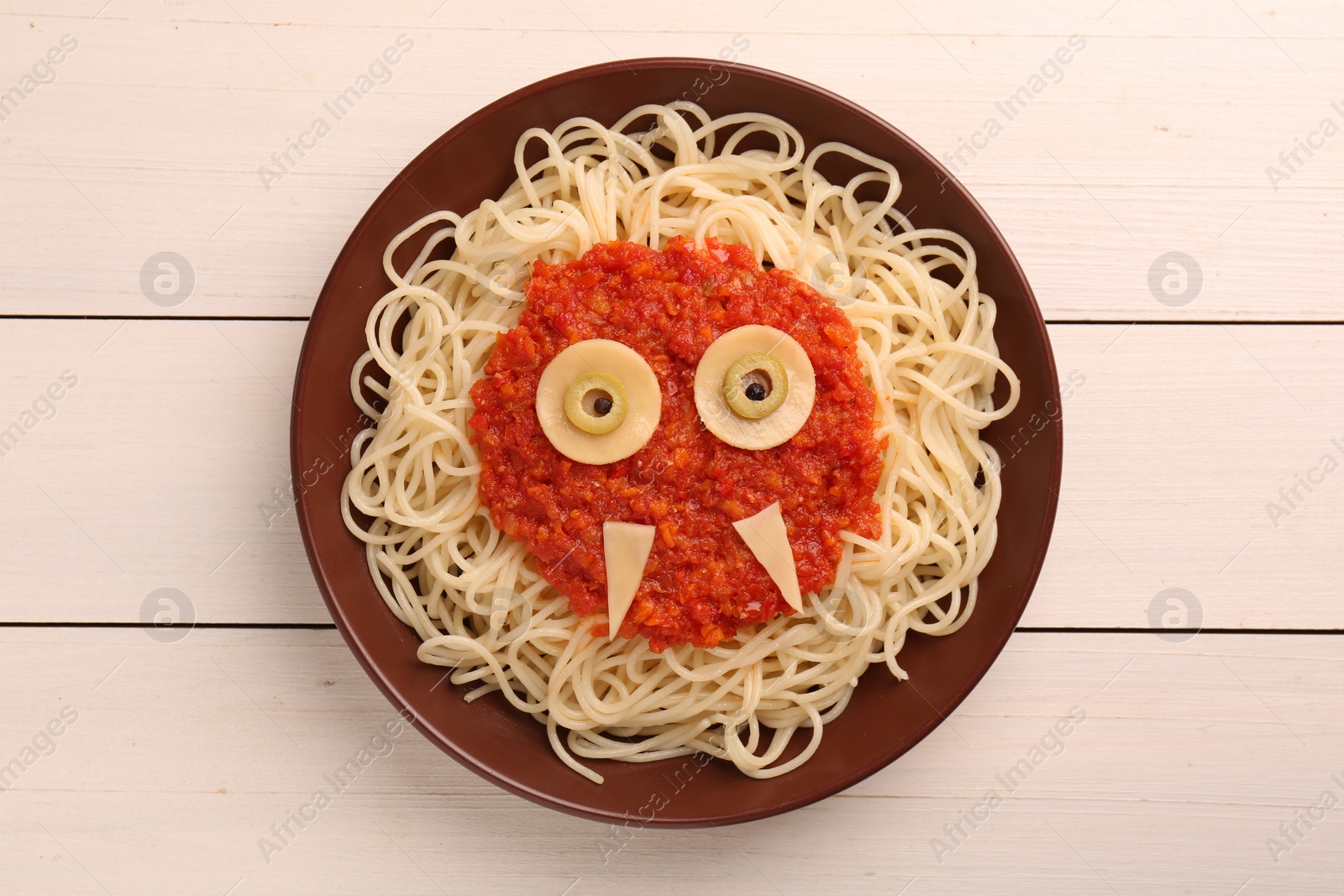 Photo of Plate with funny monster made of tasty pasta on white wooden table, top view. Halloween food