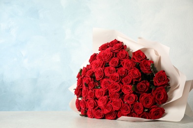 Photo of Luxury bouquet of fresh red roses on light table, space for text